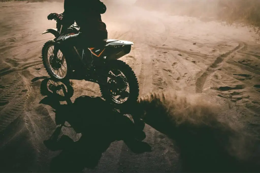 A motorbike kicking up dust on loose sand during pre-ride training.