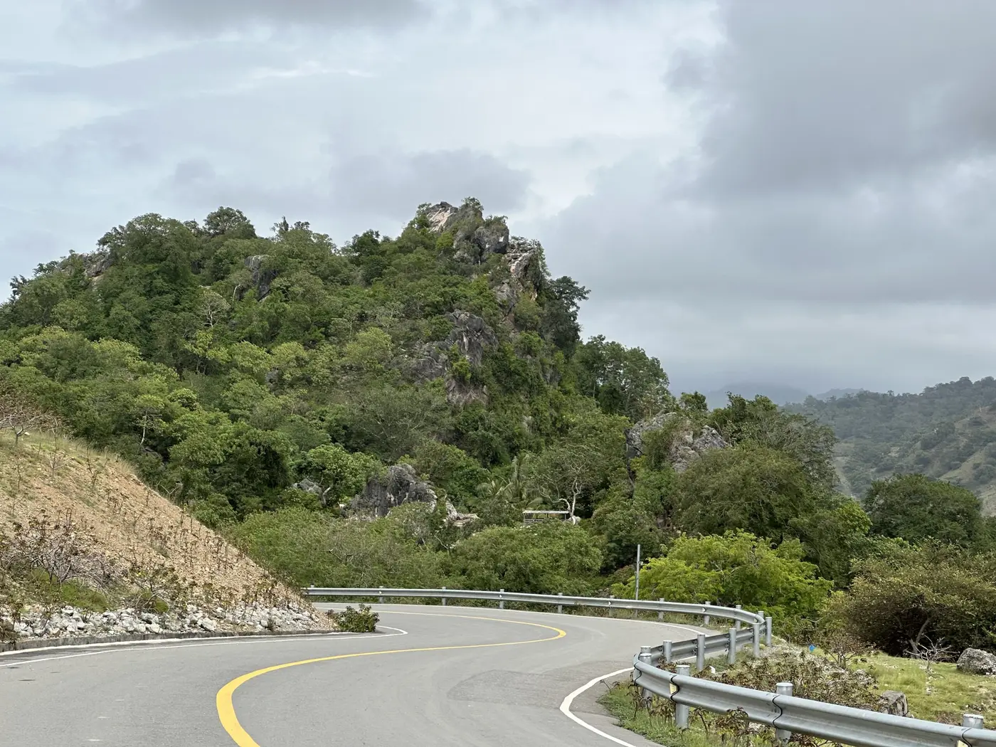 A sealed road curving through green rock outcrops under a cloudy sky.