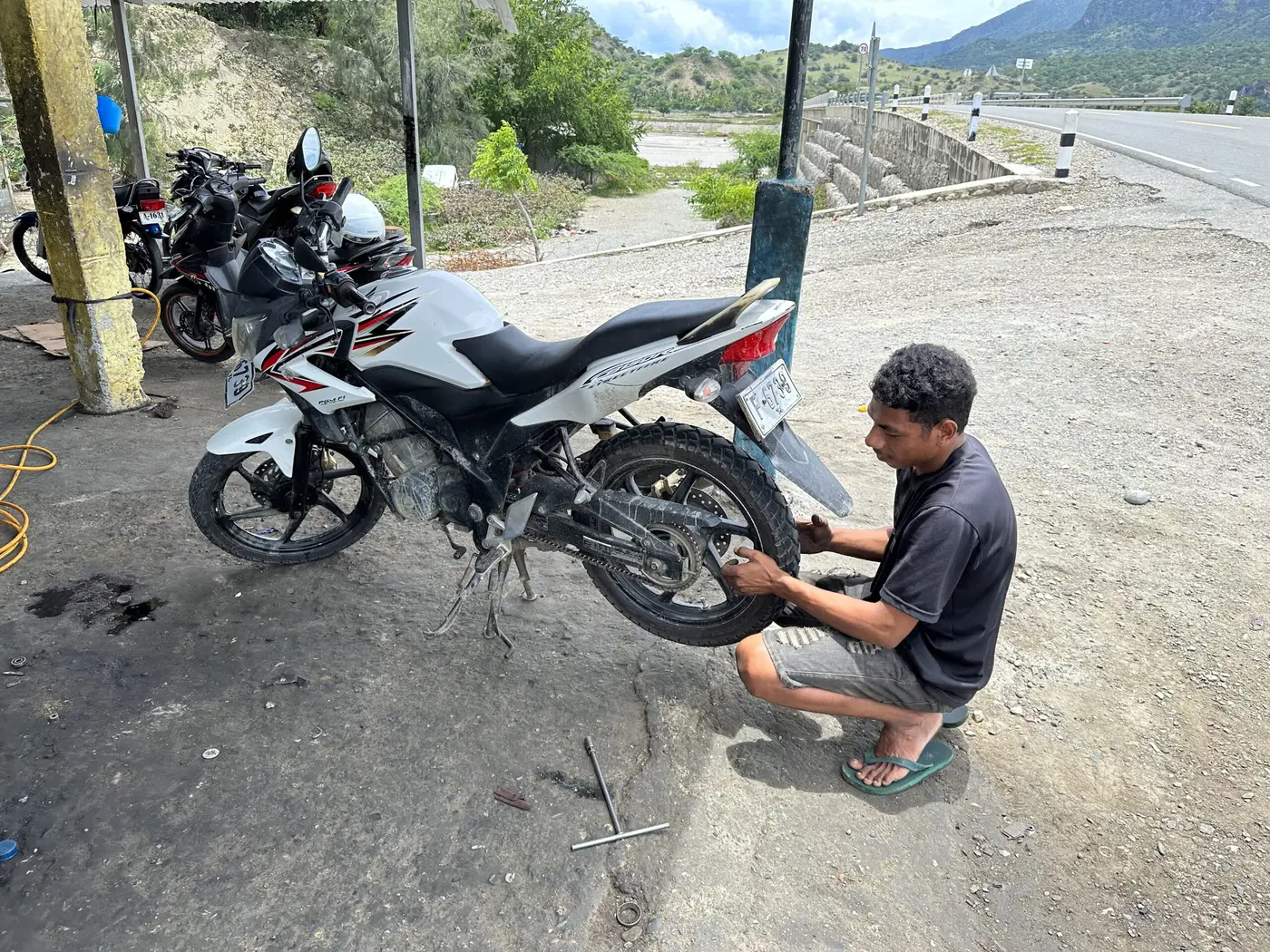 A roadside helper re-tensioning the motorbike’s loose chain in Timor-Leste.